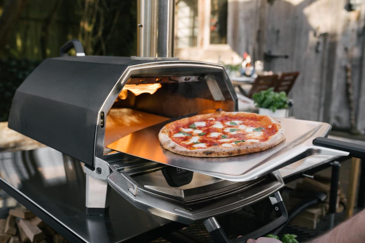 OONI pizza oven baking a pizza in an outdoor garden setting.