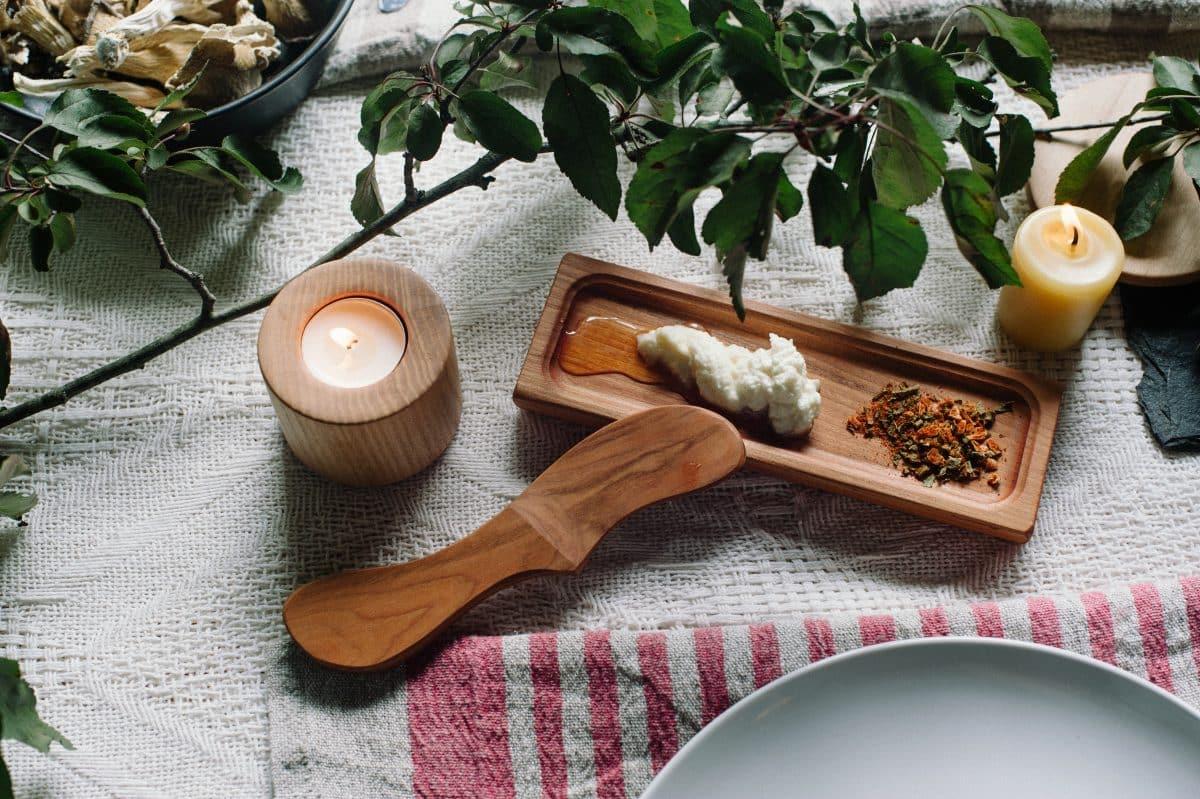 Wooden spoon and tray on a fabric background with candles and herbs.